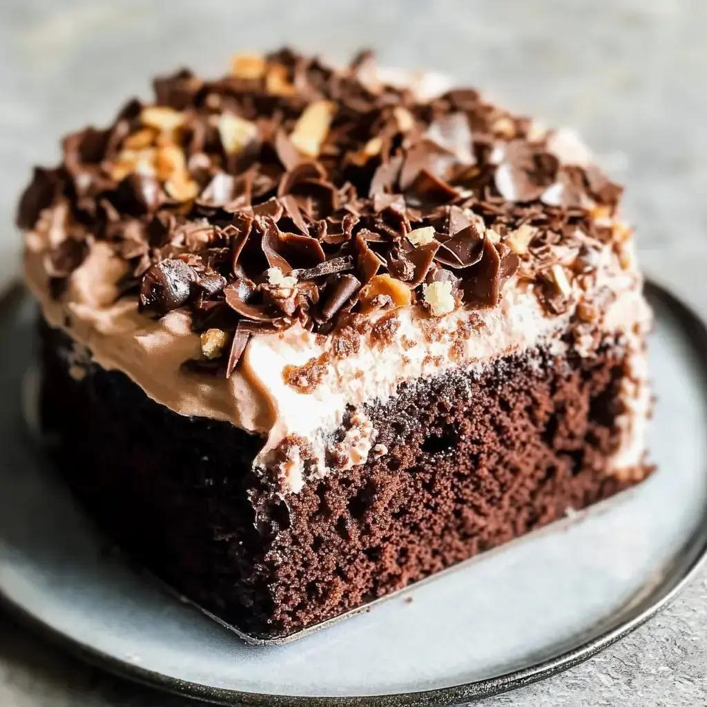 Chocolate cake covered with cream and candy pieces sitting on a gray plate.
