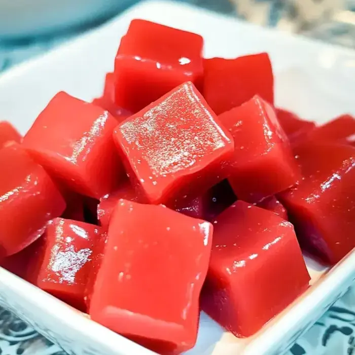 Close-up of shiny red gelatin cubes stacked on a white plate.