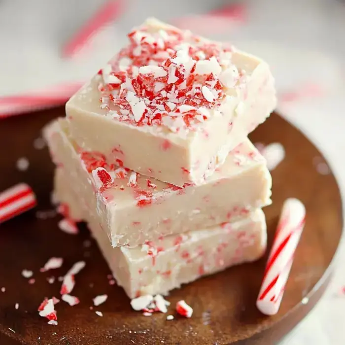 A closeup of white peppermint fudge with candy cane bits on top, sitting on a wooden board with mini candy canes nearby.