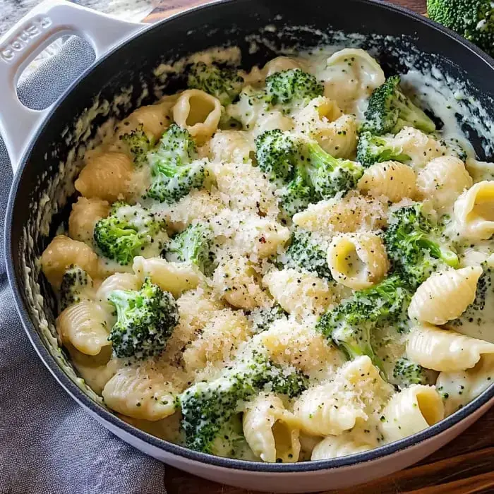Pasta with broccoli and creamy sauce, sprinkled with cheese and pepper in a big pot.