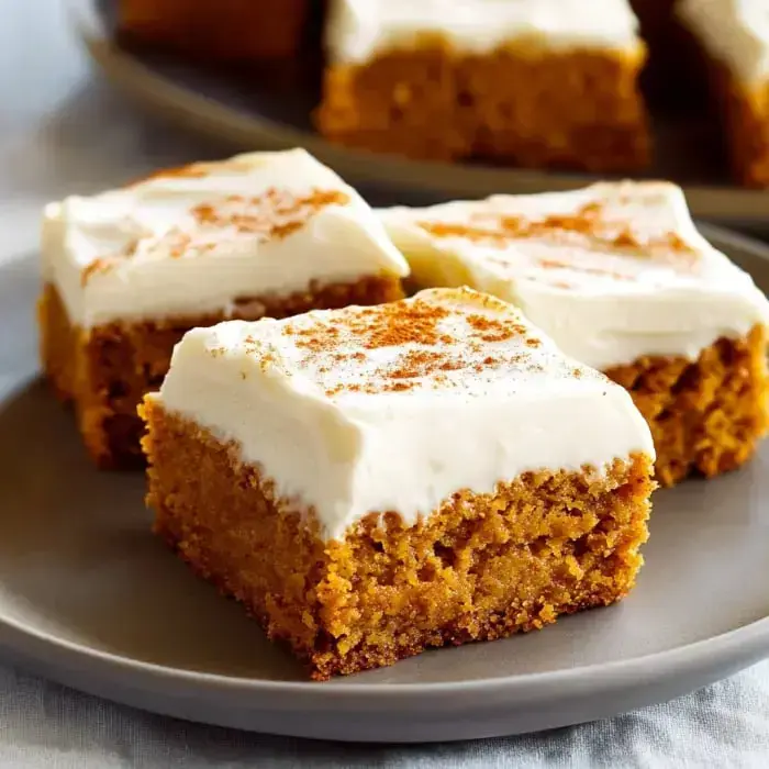 Pumpkin bars on a plate with thick frosting and a sprinkle of cinnamon.