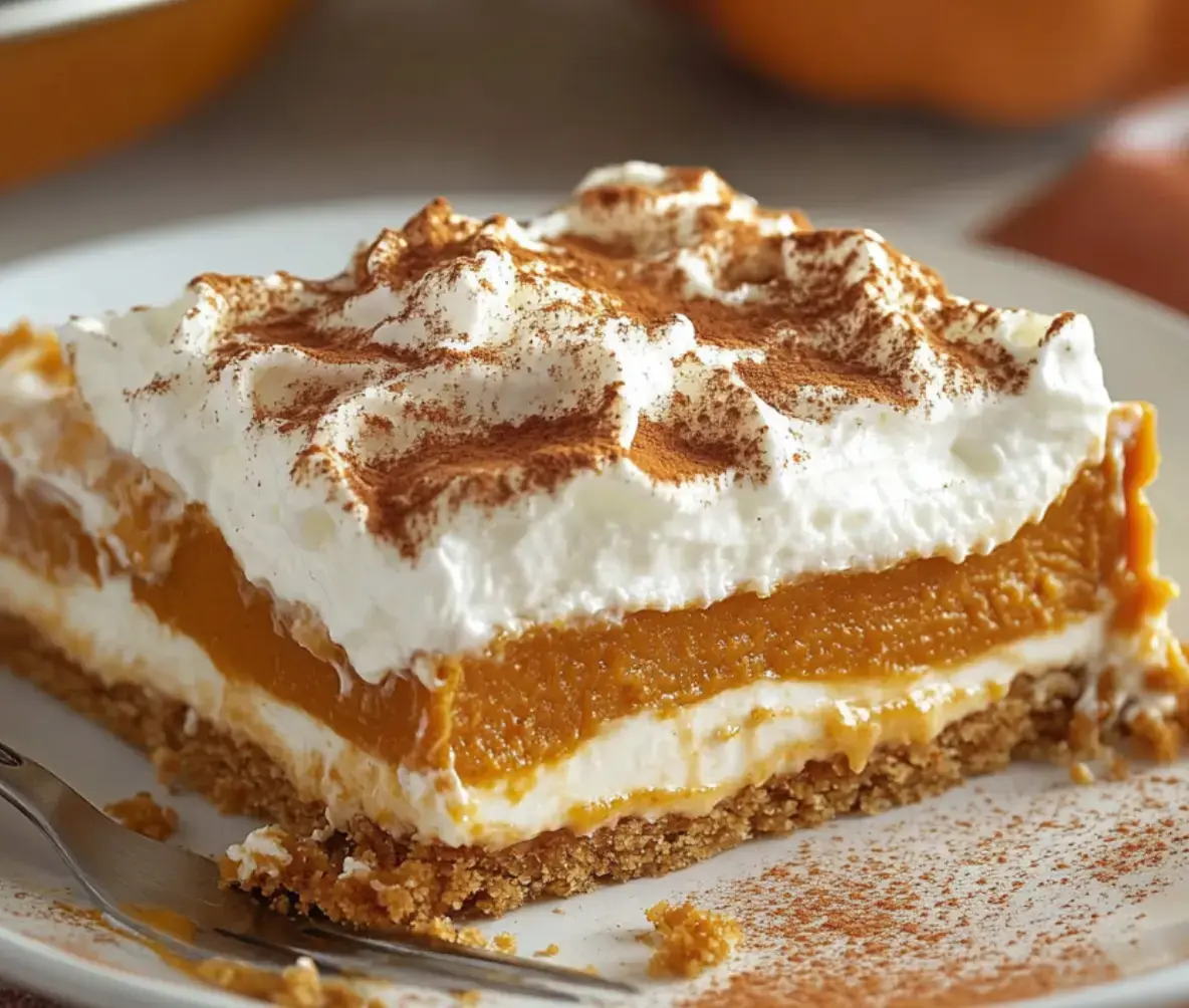 Pumpkin layered treat with fluffy whipped cream and a crunchy crust, dusted with cinnamon.