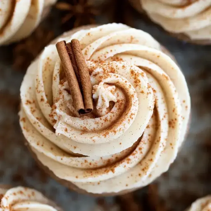 Frosted cupcake up close, with cinnamon sticks stuck on top and a sprinkle of cinnamon.