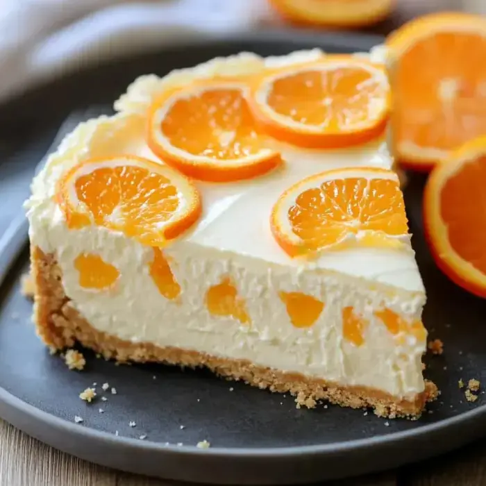 Slice of creamy orange cheesecake with orange slices on a black plate.