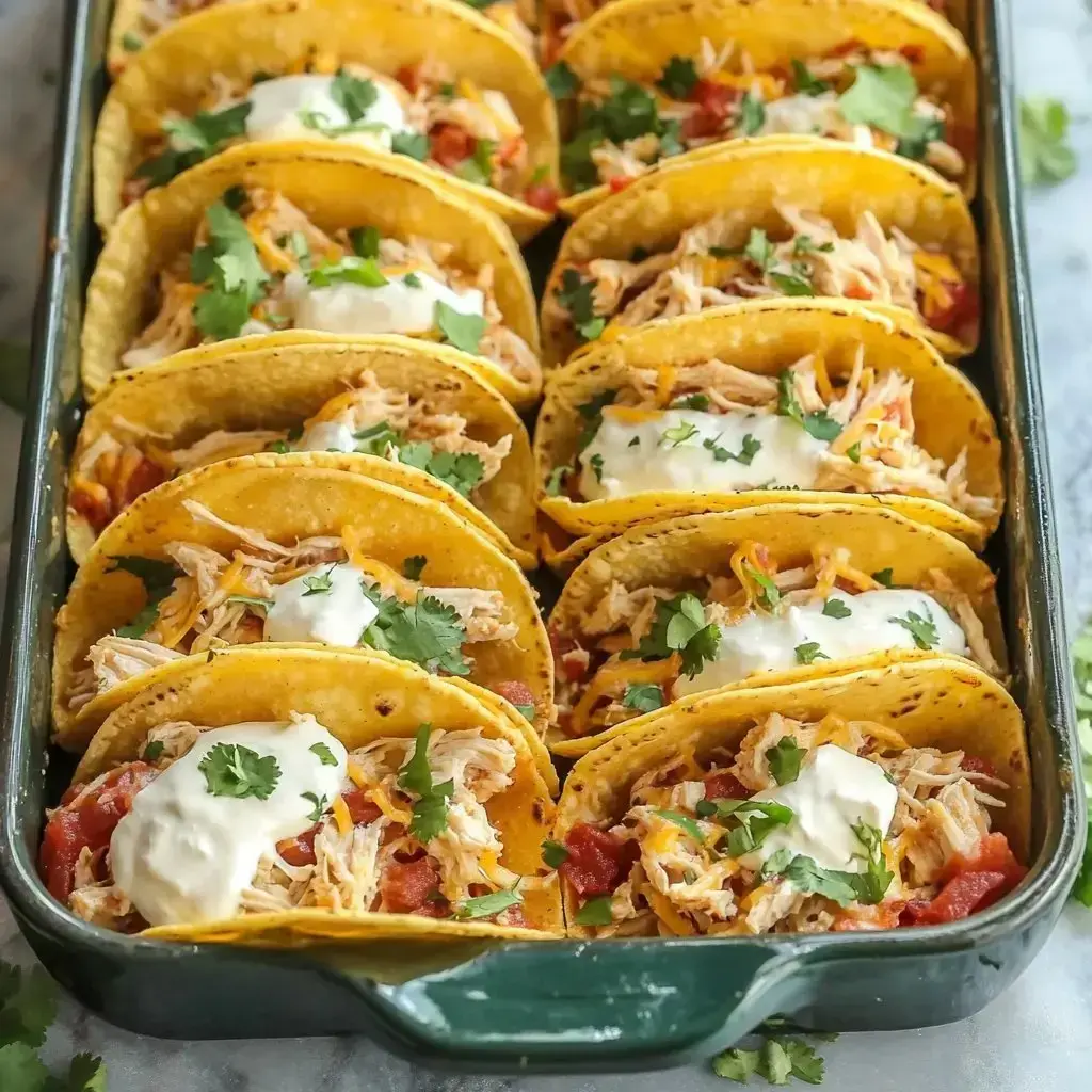 A dish of stuffed tacos loaded with chicken chunks, melted cheese, chopped tomatoes, dollops of sour cream, and sprinkled with fresh cilantro.