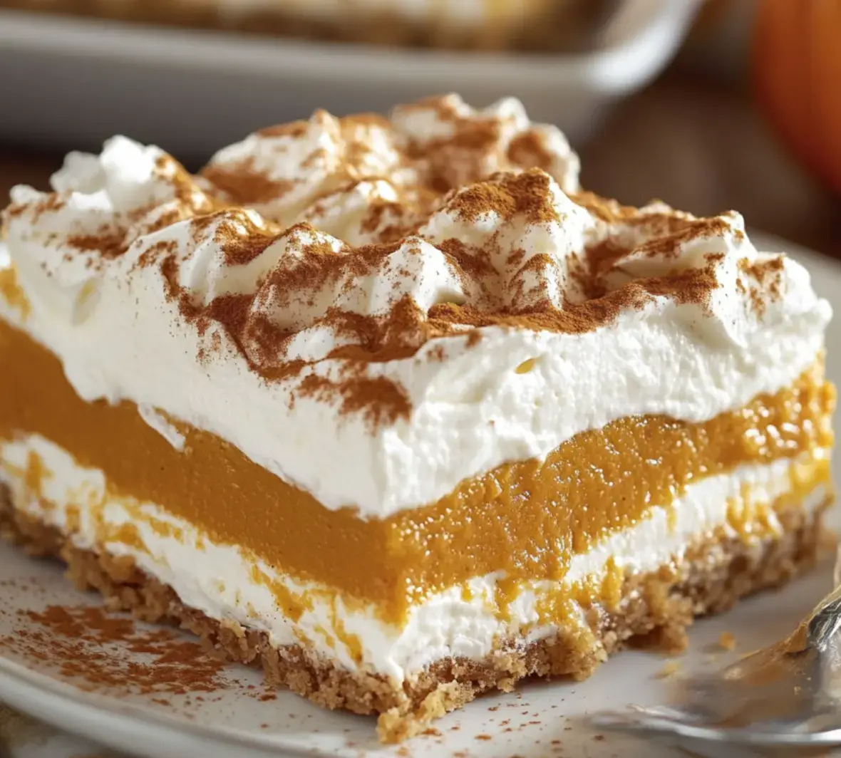A big close up showing a pumpkin slice packed with whipped cream and a thick crumbly crust. There's cinnamon dusted over the top.