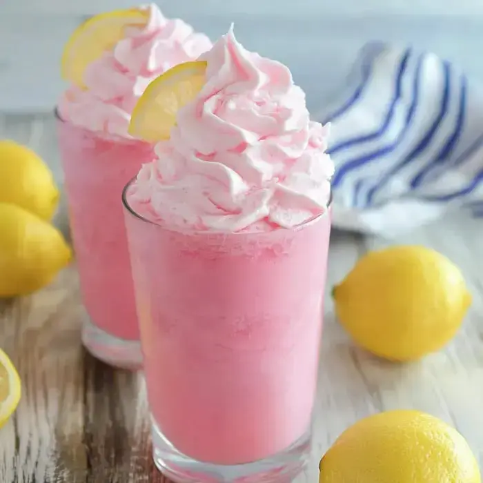 Chilled pink drinks with fluffy cream and lemon garnishes, sitting next to fresh lemons on a wood board.