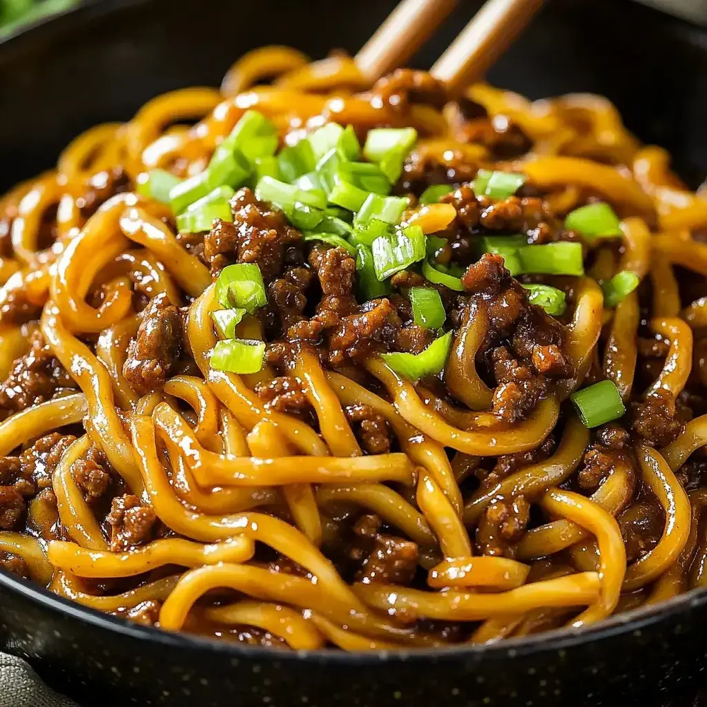 Super close photo of noodles topped with ground meat with green onion sprinkled over everything.
