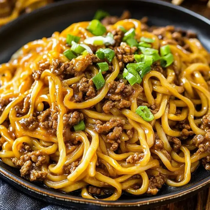 Close-up plate loaded with noodles, chopped green onion, and browned ground beef.
