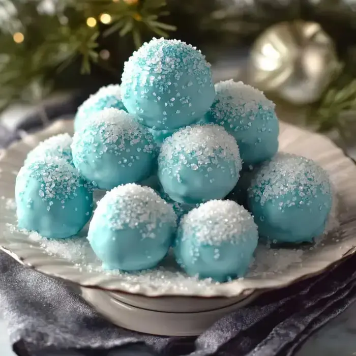A festive plate of light blue sugar-coated dessert balls arranged like snow with holiday greens around.