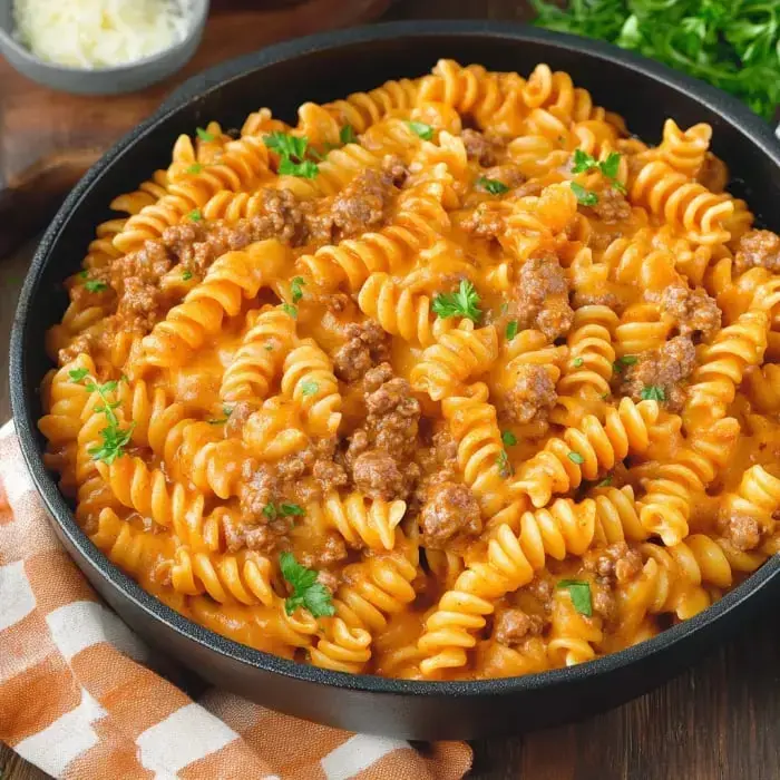 A close shot of spiral pasta in a rich tomato-cream sauce with ground beef, garnished with parsley.