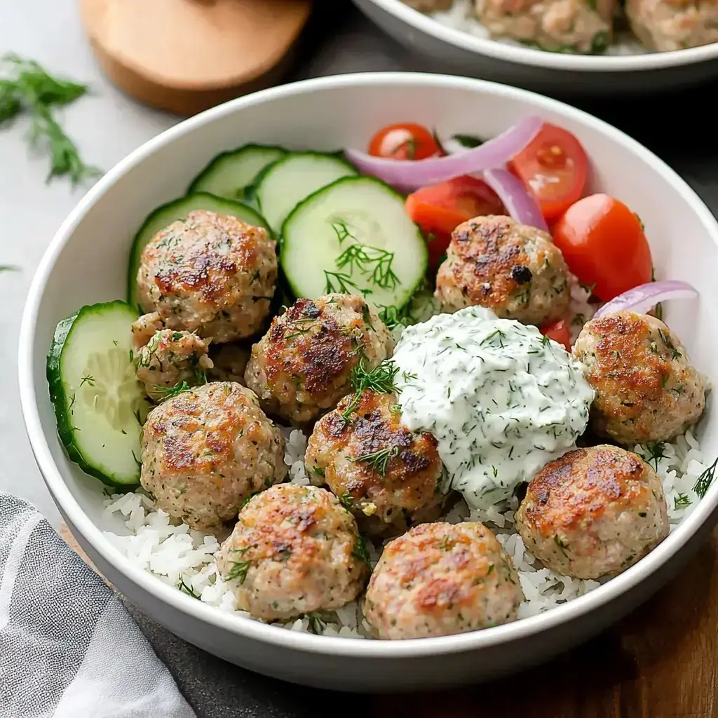 Golden meatballs with rice, veggies, and a dollop of creamy tzatziki in a bowl.