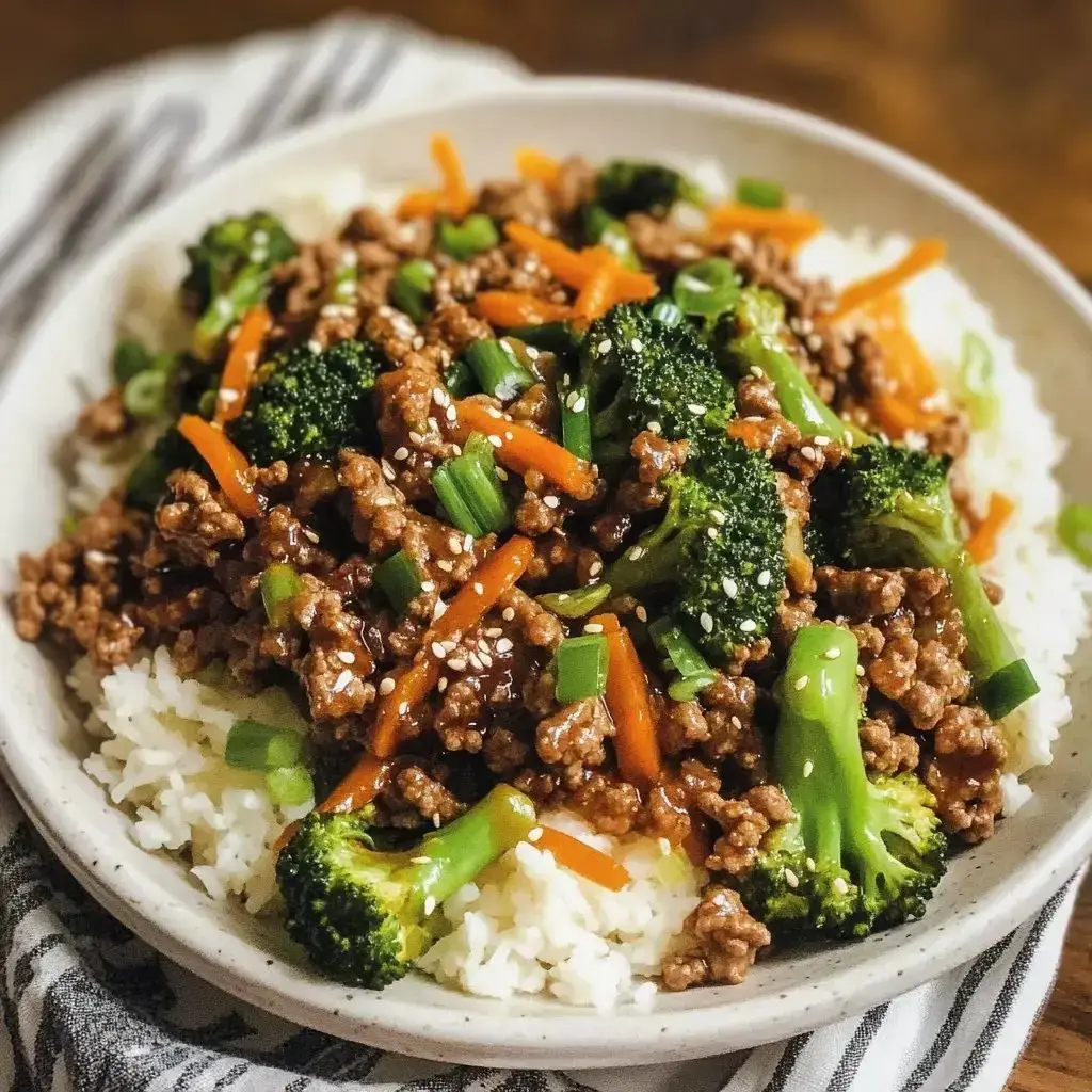 A rice bowl topped with stir-fried meat, broccoli, carrots, and green onions, sprinkled with sesame seeds.