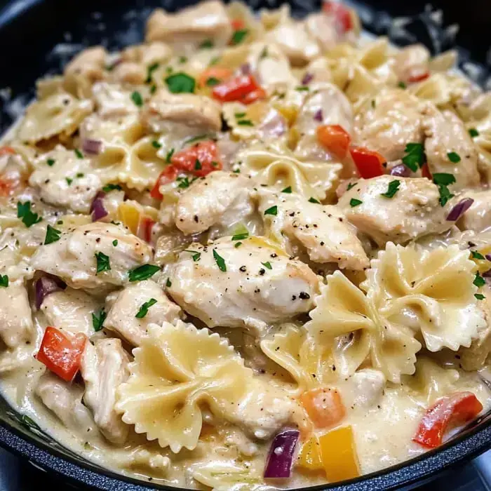 Close-up of creamy bow tie pasta and chicken, topped with parsley and colorful veggies.