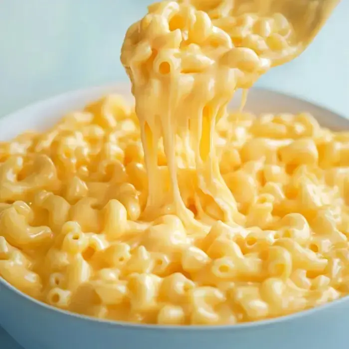 A spoon pulling up gooey macaroni smothered in cheese from a bowl.
