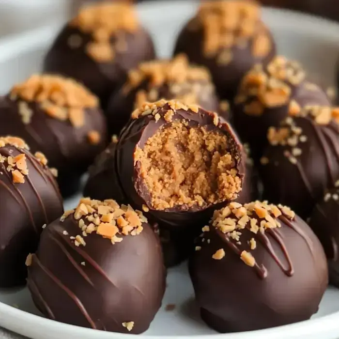 Close-up of chocolate-covered treats, some sprinkled with nuts, showing a creamy peanut butter filling inside one with a bite taken out.
