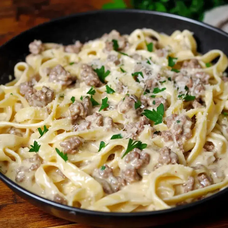 A bowl packed with creamy fettuccine, ground beef, and fresh herbs on top.