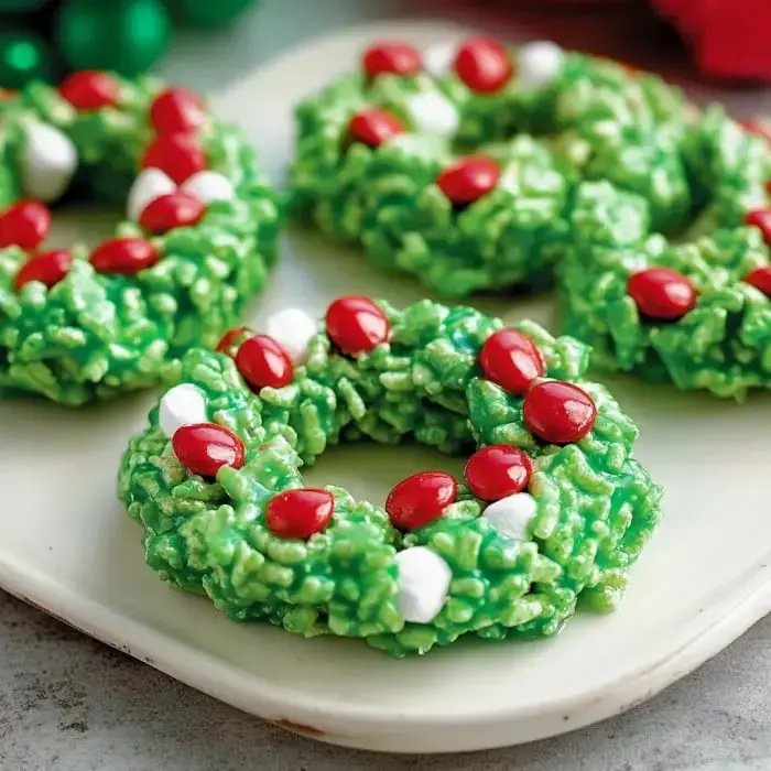 A festive plate with bright green treats shaped like little wreaths, topped off with red candies and some white marshmallows.