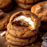 A pile of baked ginger treats with creamy centers showing where someone took a bite, with more cookies scattered around.